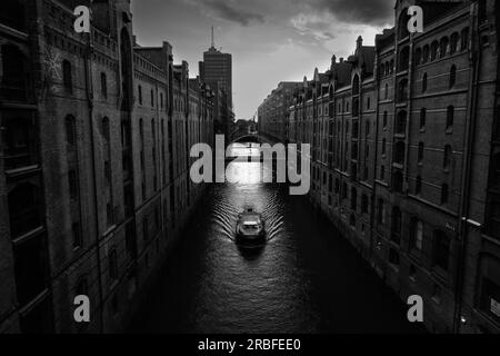 Bateau sur le canal Kehrwiederfleet dans le quartier des entrepôts Speicherstadt de Hambourg en noir et blanc Banque D'Images