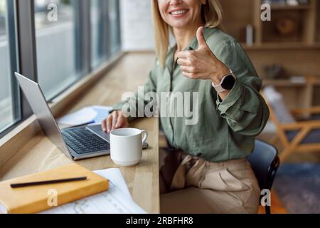 Gros plan os femme d'affaires travaillant sur ordinateur portable et montrant le pouce vers le haut dans le café. Concept de travail à distance Banque D'Images