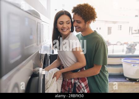 Homme romantique serrant femme chargeant la machine à laver à la laverie automatique Banque D'Images
