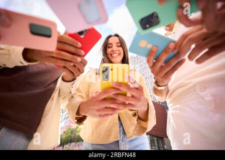 Fille caucasienne regardant le téléphone portable heureux. Vue à angle bas des amis du groupe accro à la technologie. Banque D'Images