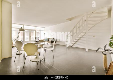 un salon avec quelques chaises et un escalier menant au deuxième étage dans un appartement qui a été peint en blanc Banque D'Images