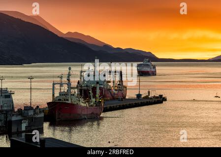 Lever de soleil très coloré dans le port d'Ushuaia, avec un couple de bateaux amarrés au premier plan et un autre s'approchant au loin Banque D'Images