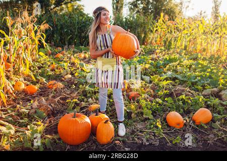 Récolte de citrouilles. Jeune femme fermière cueillant la récolte d'automne de citrouilles à la ferme mettant des légumes sur pile. Agriculture. Banque D'Images