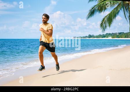 Jeune homme d'exécution sur la rive de la mer de plage tropicale. Mode de vie sain et sport concept Banque D'Images