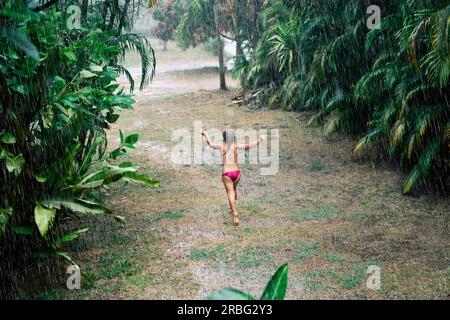 Jolie petite fille profiter de la pluie et de la danse dans la rue sous la pluie en été. Le bonheur des enfants, la joie et le plaisir Banque D'Images