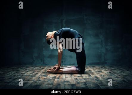 Young woman practicing yoga chameau faisant poser dans une pièce sombre. Ustrasana asana. Le bien-être et mode de vie sain Banque D'Images