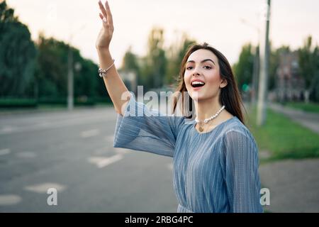 Une jeune jolie femme qui agite des mains levées pour faire de la randonnée ou accueillir des amis sur fond de ville. Bonjour, concept de salutation Banque D'Images