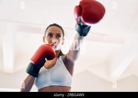 Boxer féminin dans des gants de boxer pratiquant ses coups de poing. Femme athlétique faisant un coup direct. Concept sport Banque D'Images