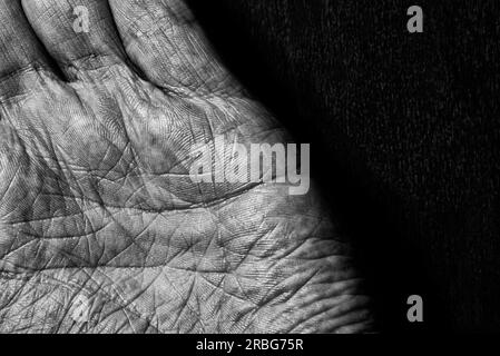 Image en noir et blanc de mains masculines âgées sur un fond sombre. Détail de la paume de la main Banque D'Images