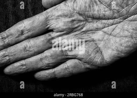 Image en noir et blanc de mains masculines âgées sur un fond sombre. Détail de la paume de la main Banque D'Images