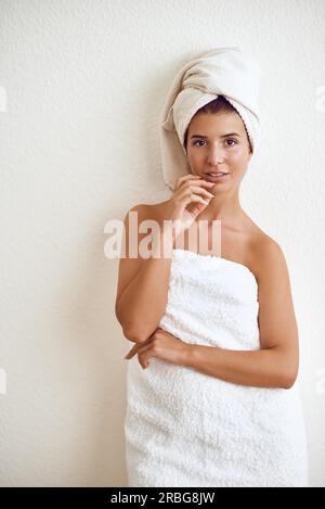 Souriant heureux sain attrayant jeune femme enveloppé dans une serviette blanche moelleuse propre debout contre un mur blanc conceptuel de l'hygiène personnelle et Banque D'Images