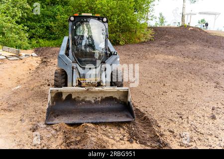 mini chargeur avec godet. Une chargeuse avec un godet dégage le site pour la construction. Travaux d'amélioration foncière sur le territoire. Machine pour le déplacement du sol, sa Banque D'Images