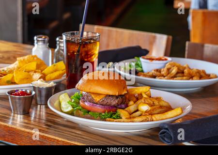 Hamburger maison avec bœuf, oignon, tomate, laitue et fromage. Burger frais closeup sur la table rustique en bois avec frites de pommes de terre, bière et chips. Banque D'Images