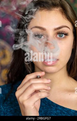 Une belle mannequin brune fume de la marijuana dans l'intimité de sa propre maison Banque D'Images