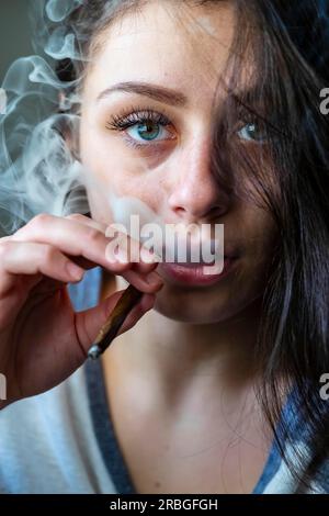 Une belle mannequin brune fume de la marijuana dans l'intimité de sa propre maison Banque D'Images