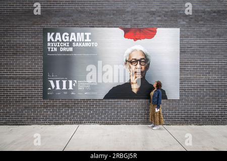 Captivé par le génie de Ryuichi Sakamoto, un fan dévoué regarde un panneau publicitaire pour promouvoir Kagami, une expérience de concert virtuel révolutionnaire. Banque D'Images