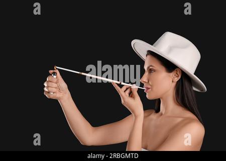 Femme utilisant le long porte-cigarette pour fumer sur fond noir Banque D'Images