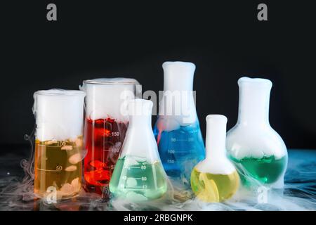 Verrerie de laboratoire avec liquides colorés et vapeur sur fond noir. Réaction chimique Banque D'Images