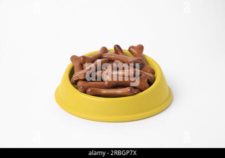 Bol jaune avec des biscuits de chien en forme d'os sur fond blanc Banque D'Images