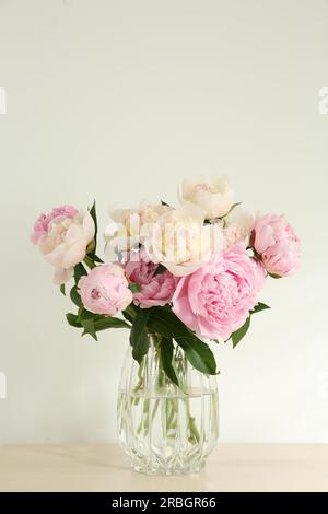 Bouquet de belles pivoines dans un vase en verre sur table beige Banque D'Images