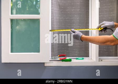 Homme mesurant le cadre de fenêtre en bois pour l'installation moustiquaire de filet. Banque D'Images