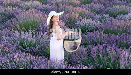 adolescente positive avec de la lavande tenant un bouquet de fleurs dans une robe marchant dans le parc de lavande. Banque D'Images