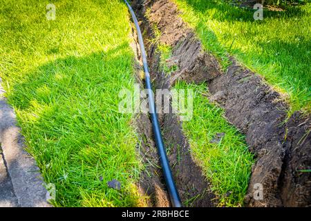 Un fossé creusé dans la pelouse pour la pose de tuyaux et l'installation d'irrigation. Sol sous pelouse verte et système de racines d'herbe Banque D'Images