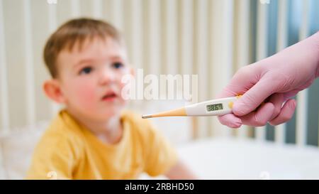 L'infirmière prend la température de l'enfant à l'aide d'un thermomètre avant d'administrer le médicament. Enfant âgé d'environ deux ans (un an onze mois) Banque D'Images