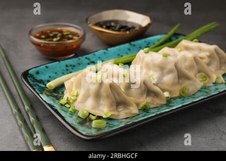 Délicieux gyoza (boulettes asiatiques) avec oignons verts et baguettes sur la table grise, gros plan Banque D'Images