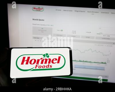 Personne tenant un téléphone portable avec le logo de la société alimentaire américaine Hormel Foods Corporation sur l'écran devant la page Web. Concentrez-vous sur l'affichage du téléphone. Banque D'Images