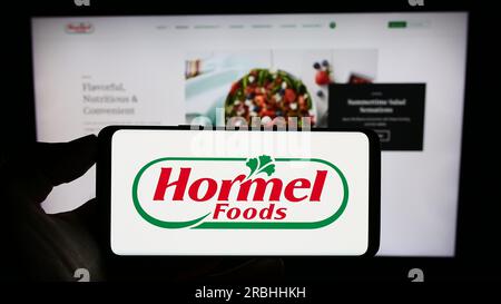 Personne tenant un smartphone avec le logo de la société alimentaire américaine Hormel Foods Corporation sur l'écran devant le site Web. Concentrez-vous sur l'affichage du téléphone. Banque D'Images