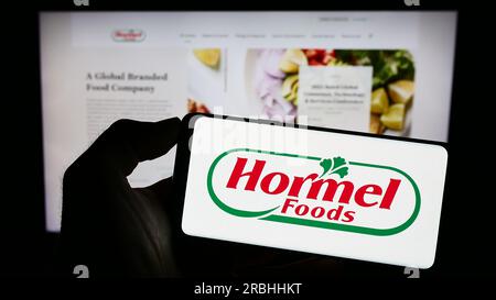 Personne tenant le téléphone portable avec le logo de la société alimentaire américaine Hormel Foods Corporation sur l'écran devant la page Web de l'entreprise. Concentrez-vous sur l'affichage du téléphone. Banque D'Images