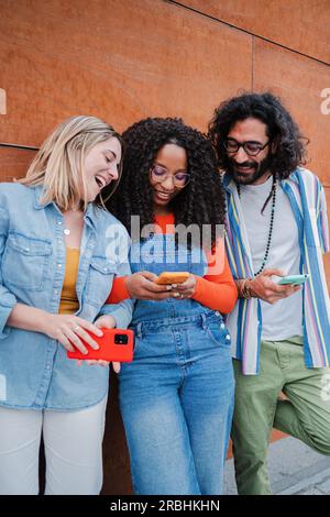 Portrait vertical. Femme utilisant son téléphone portable montrant ses amis des messages texte amusants ensemble. Groupe souriant d'amis s'amusant à naviguer sur Internet avec smartphone, jeunes avec téléphone portable. Photo de haute qualité Banque D'Images