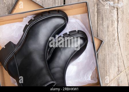 les bottes hautes noires pour femmes avec des semelles épaisses sont dans une boîte sur une vieille planche sur la rue, les chaussures d'hiver pour femmes, les chaussures Banque D'Images