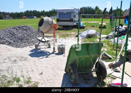 Gros plan sur le mélangeur de béton, mortier de ciment mélange avec la roue de construction barrow sur le chantier de construction de maison. Banque D'Images