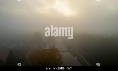 Une photographie aérienne enchanteresse capturant un matin brumeux au-dessus d'un canal serpentant à travers une forêt d'automne richement colorée. L'image respire un sentiment de tranquillité et dépeint une belle image du côté serein de la nature pendant la saison d'automne. Vue aérienne : matin brumeux sur Forest Canal en automne. Photo de haute qualité Banque D'Images