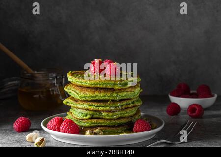 Pile de crêpes maison avec thé matcha, framboises fraîches, pistaches et miel sur fond noir Banque D'Images