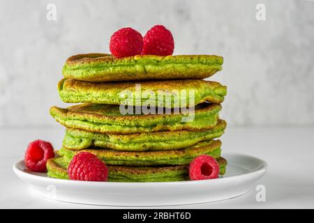 Pile de crêpes maison avec thé matcha, framboises fraîches, pistaches sur fond blanc Banque D'Images