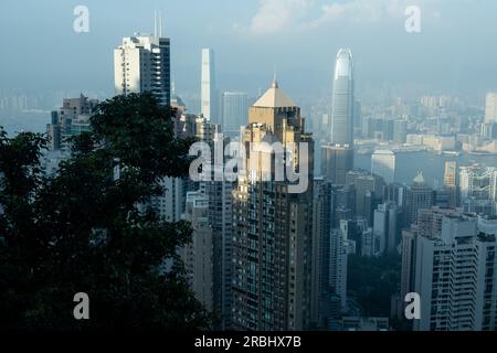 Vues incroyables sur la ville depuis le Lugard Road Lookout sur Victoria Peak, Hong Kong, un soir d'été alors que la dernière lumière du jour frappe les tours. Banque D'Images