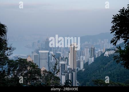 Vues incroyables sur la ville depuis le Lugard Road Lookout sur Victoria Peak, Hong Kong, un soir d'été alors que la dernière lumière du jour frappe les tours. Banque D'Images