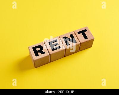 Le mot Louer sur des cubes en bois sur fond jaune. Rechercher un logement à louer ou à louer. Le concept de location. Investissements. Banque D'Images