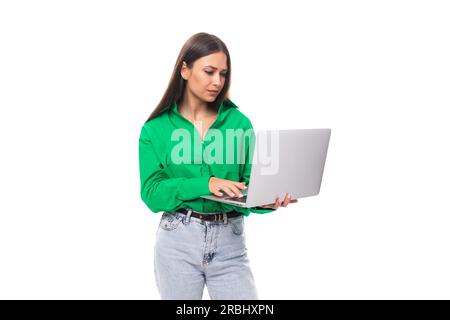 Une jeune femme d'affaires au poil long brunette bien soignée dans une chemise verte travaille dans la sphère INFORMATIQUE sur un fond blanc avec un espace de copie Banque D'Images