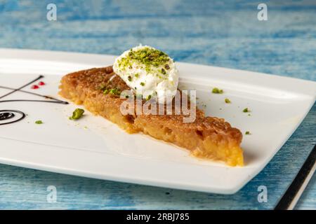 Dessert turc ekmek kadayifi avec crème de lait et pistache sur une assiette en porcelaine blanche Banque D'Images