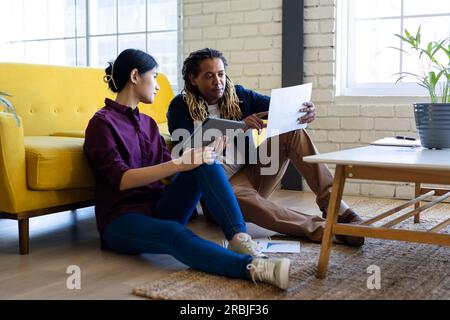 Deux collègues d'affaires occasionnels avec tablette et document assis sur le sol dans le bureau parlant. Travail d'équipe, travail, affaires, communication et occasionnel Banque D'Images