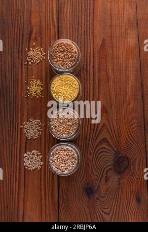 Grains de céréales dans des bocaux en verre sur fond en bois. Collection de différents gruaux vue de dessus orge, avoine, millet et blé. Aliments complets avec f élevé Banque D'Images