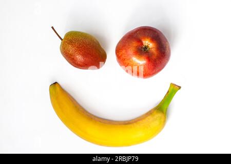 Banane fraîche, pomme, poire comme visage souriant. Concept de petit déjeuner sain créatif sur fond blanc flatlay.Vitamins minéraux, fibres alimentaires riches Banque D'Images