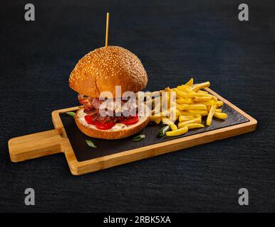 Savoureux hamburger avec des frites servies sur une planche d'ardoise Banque D'Images