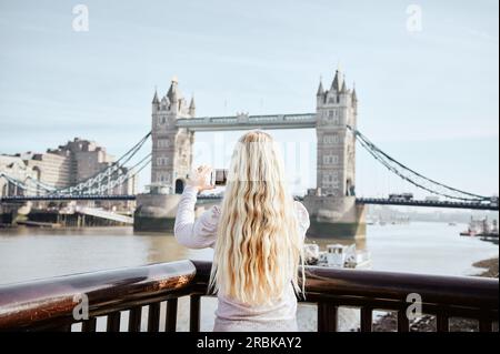 Femme blonde avec les cheveux ondulés prenant la photo de Tower Bridge Banque D'Images