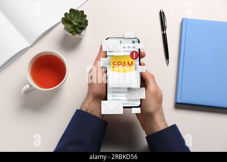 Message d'avertissement anti-spam, illustrations d'enveloppes sortant de l'écran de l'appareil. Homme utilisant le logiciel de messagerie sur smartphone à la table, vue de dessus Banque D'Images