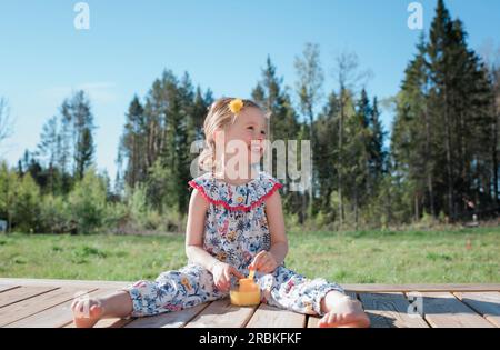 portrait d'une jeune fille assise dehors mangeant avec une fleur dans les cheveux Banque D'Images